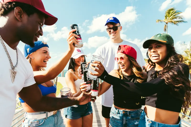 A group toasting with GameDay Spiked cans on the sand