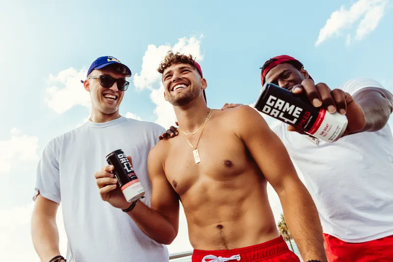 Friends in team caps holding up GameDay Spiked cans